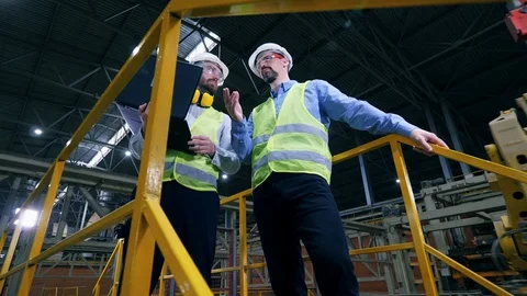 Workers stand in a factory interior, checking equipment. Video stock 118654835