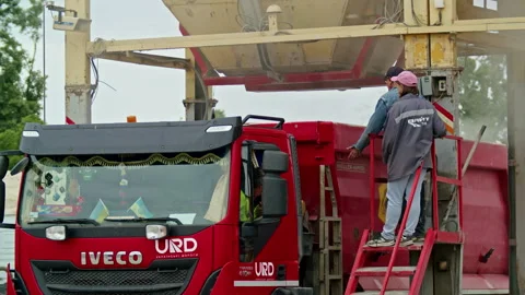 Workers supervising the loading of bulk materials into a red dump truck at an Stock Footage 304314496