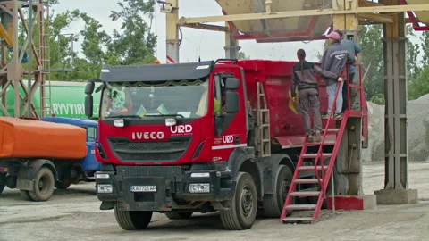 Workers supervising the loading of bulk materials into a red dump truck at an 스톡 동영상 304314759