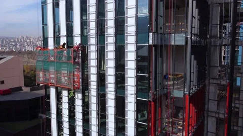 Workers on the suspended cradle are assembling the skyscraper exterior Stock Footage 168555650