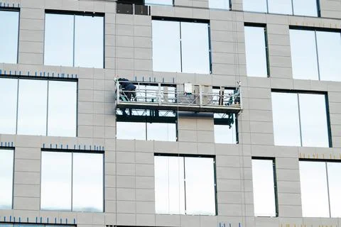 Workers on a suspended platform installing facade panels on a modern skyscrap Stock Photos