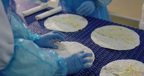 Workers topping flatbread with grated cheese on blue conveyor, Overhead View Stock Footage 340034960