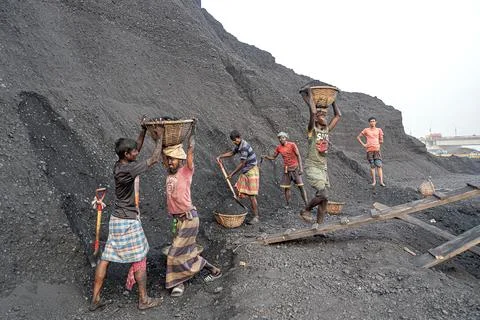 Workers transport coal in baskets at a mining site near a industrial area. Foto stock