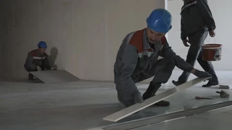 Workers in uniform and safety helmets lay tiles in a house under construction Stock Footage 321003993
