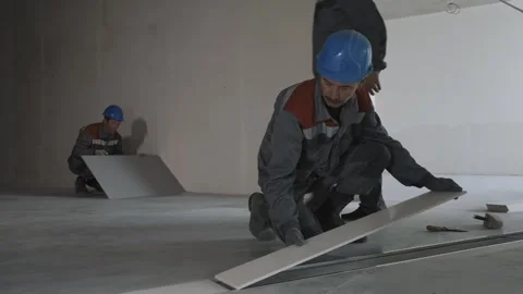 Workers in uniform and safety helmets lay tiles in a house under construction Stock Footage 321004356