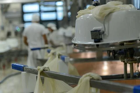 Workers in uniform are seen in the background of a cheese-making process, w.. Stock Photos
