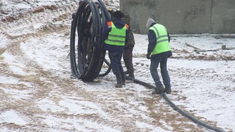 Workers unwind a pipe for a cable at a construction site, background, industry Stock Footage 129935422