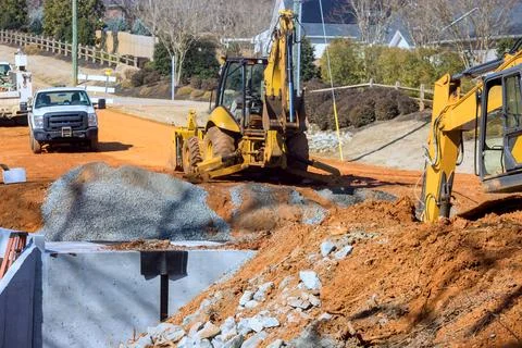 Workers use heavy machinery to move dirt gravel as road construction occurs i Stock Photos