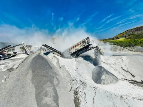 Workers use large machines to process granite at a quarry. Dust rises as they Stock Photos