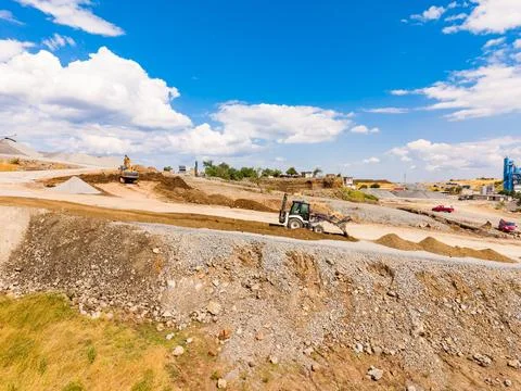 Workers use machinery to move earth and stone at a granite quarry location. H Stock Photos