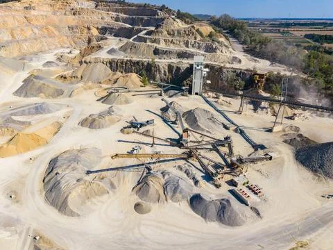 Workers use machines to move and sort materials in a large quarry with piles  Stock Photos