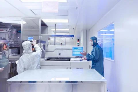 Workers using manufacturing machinery in flexible electronics factory clean room Stock Photos