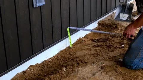 Workers using tape measure and spade to move dirt near a house foundation Stock Footage 153861728