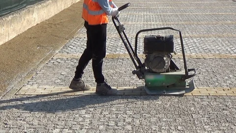 Workers using a vibro-compacting plate to compact self-locking blocks in thei Stock-Footage 105879886