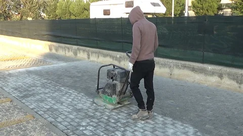 Workers using a vibro-compacting plate to compact self-locking blocks in thei Stock-Footage 107338017