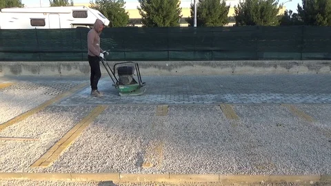 Workers using a vibro-compacting plate to compact self-locking blocks in thei Stock-Footage 107338172