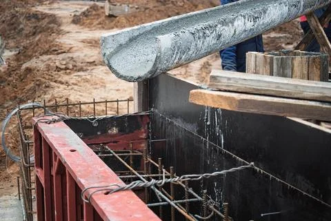 Workers utilize a concrete pump to pour wet concrete into a formwork at a con Stock Photos