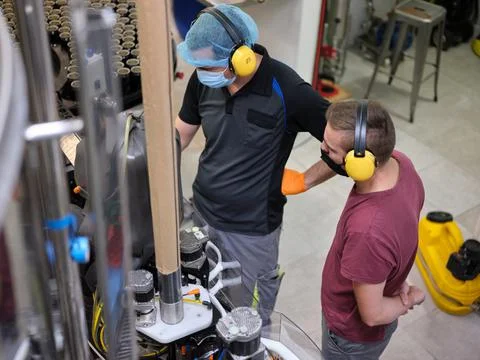 Workers wearing mask checking the machinery of a craft beer factory. Stock Photos