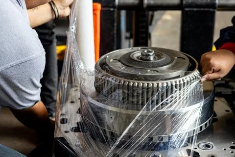 Workers Wrapping Heavy Industrial Machine Component With Plastic Film. Stock Photos