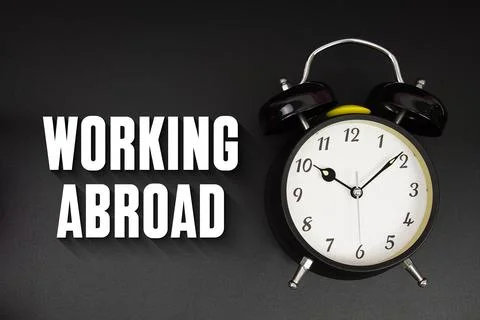 Working Abroad text with alarm clock on black background Stock Photos