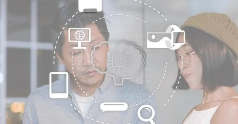 Working Asian colleagues in blue button-up and beige beanie examining AI icons Stock Photos