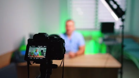 Working camera is directed on the medic sitting at desk. Doctor speaks to camera Stock Footage 333782539