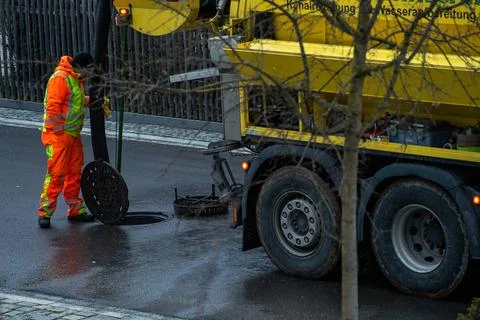 Working channel digger, doing the work at a open manhole ona wet street at the Stock Photos