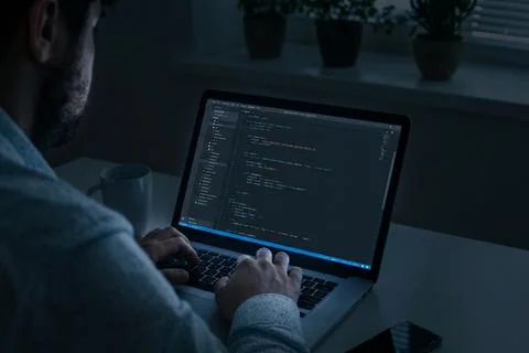 Working on coding tasks at night in a dimly lit room with a laptop Foto stock