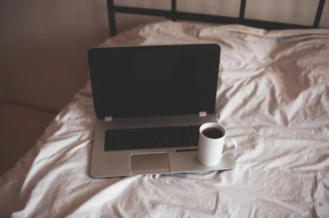 Working computer with cup of coffee in bed closeup in room. Quarantine time.  Stock-Fotos