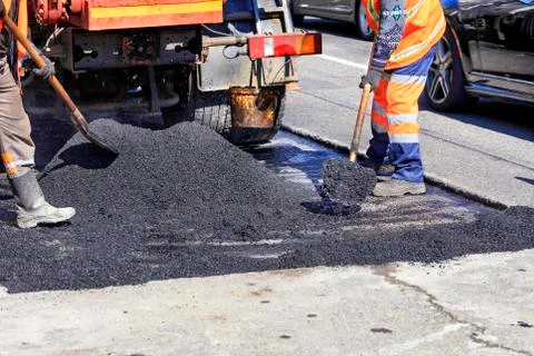 The working crew evenly distributes hot asphalt with shovels manually on the Stock Photos