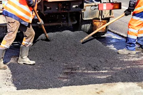 The working crew evenly distributes hot asphalt with shovels manually on the Stock Photos