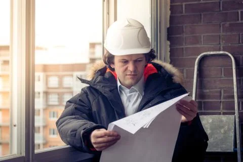 Working engineer in a white construction helmet with a project or drawing plan Stockfoto's