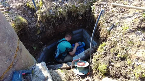 Working on equipment inside a hole at the construction site to fix plumbing on a Stock Footage 332064772
