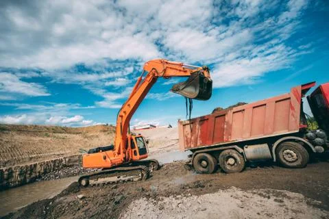 Working excavator on construction site, loading dumper truck during earthmoving Stock Photos