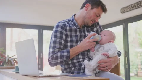Working father multi-tasking talking on mobile phone whilst feeding crying baby Stock Footage 158789528