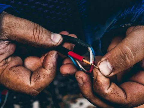 Working hands stripping and twisting colorful electrical wires, creating a Фото