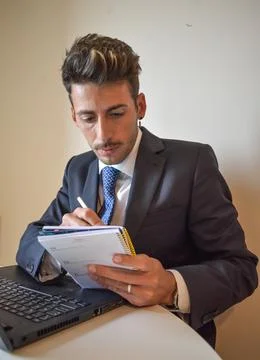 The working handsome man taking notes in the notebook while working with his  Stock Photos