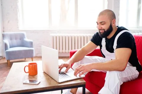 Working at home. Young man using laptop computer while sitting on sofa. Stock Photos