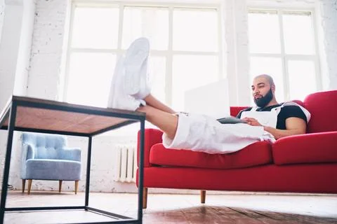 Working at home. Young man using laptop computer while sitting on sofa. Stock Photos