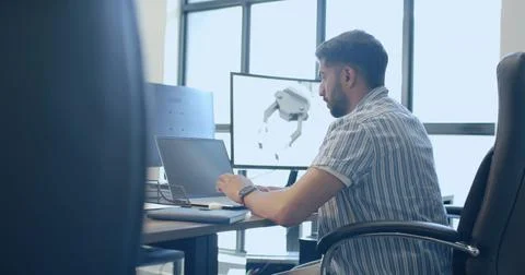 Working Indian male engineer designing 3D robotic arm at desk with laptop and Stock Photos