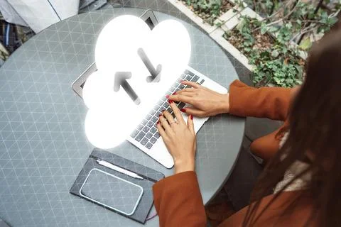 Working on a laptop with cloud upload symbol while sitting at a table outdoors 스톡 사진