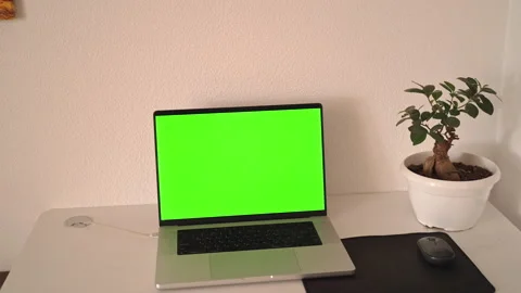 Working on a laptop at a desk with green screen background in a simple room Stock Footage 341327015