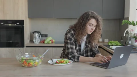 Working On Laptop In Kitchen While Eating Fresh Salad At Counter Stock Footage 311271496