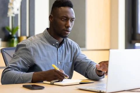 Working on laptop, man taking notes in office, focusing on task Stock Photos