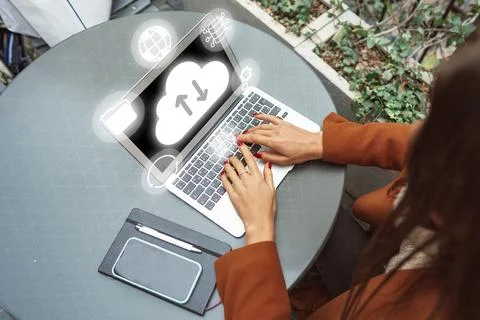 Working on a laptop at an outdoor table with cloud icons in the background 스톡 사진