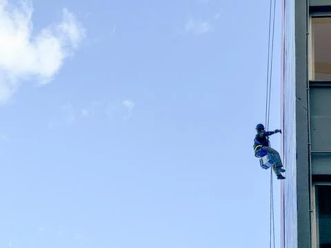 Working man abseils down to paint building Stock Photos