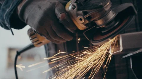 Working man grinds metal with flying sparks close up panning shot Видео 104076231