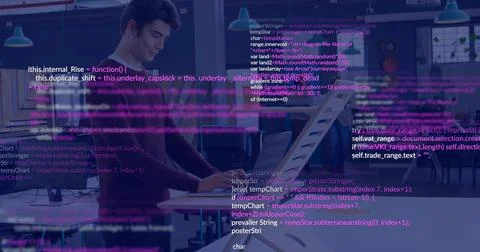 Working man at left standing desk in tech office, wearing dark sweater, code Stock Photos
