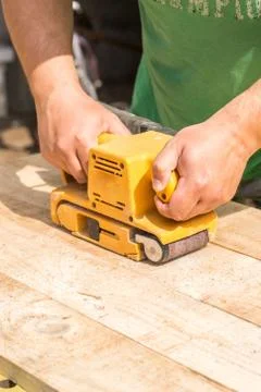 Working man with sanding machine sands wooden planks Stock Photos