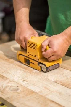 Working man with sanding machine sands wooden planks Stock Photos